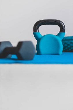 Ev jimnastik salonu ve spor salonu konsepti, kettlebell köpük silindirli mavi yoga minderi ve düşük perspektiften sığ alan derinliğinde dambıl atışı.