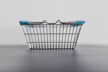 Minimalist alışveriş kavramsal natürmort, arkasında beyaz arkaplan olan yansıtıcı gri yüzeyde boş alışveriş sepeti.