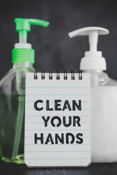 keep your hands clean to fight bacteria and viruses conceptual still-life, hand sanitizer and liquid soap next to memo with Clean your Hands text