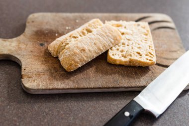 Yemek malzemeleri ve yemek hazırlama konsepti, ciabatta ekmeği yanında bıçakla tahtayı ikiye bölmek.