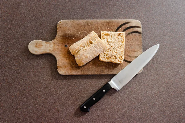 food ingredients and meal prepping concept, ciabatta bread cut in half on cutting board with knife next to it