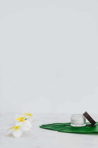 веганская природная красота без жестких химических веществ концепция, горшок крема для лица и бутылка лосьона для тела на зеленых листьях с монои цветы
