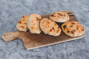 Kilerdeki sağlıklı basit yiyecekler, gri beton arka planda kesim tahtasındaki küçük ev yapımı ekmek ruloları.