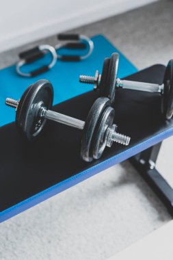 Spor salonu ve online fitness konsepti, spor salonundaki dambıllar ve yoga minderindeki şınav kulpları ile evden spor salonu.