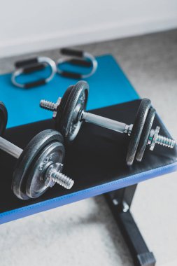 Spor salonu ve online fitness konsepti, spor salonundaki dambıllar ve yoga minderindeki şınav kulpları ile evden spor salonu.