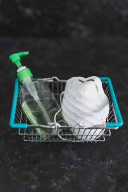 Market alışverişi ve virüs salgınları sırasında markette nasıl güvende kalınacağı, yüz maskeli alışveriş sepeti ve bulaşıcı hastalıklardan korunmak için el dezenfektanı.