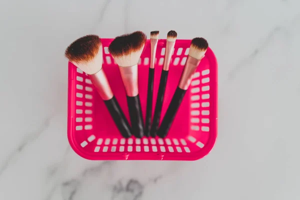beauty industry and essential products concept, pink shopping basket with variety of make-up brushes in it for face and eye make-up