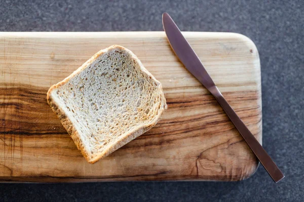 healthy food ingredients, piece of toasted bread on cutting board with knife next to it