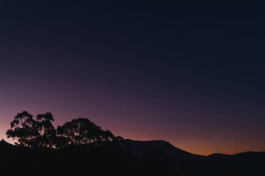 Günbatımı gökyüzü maviden mora, turuncu gradyan renklere (düzenlenmemiş) ve Tazmanya, Avustralya tepeleri üzerinde ay okaliptüs ağacı siluetleriyle