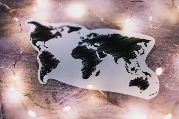 world map surrounded by fairy lights on concrete desk shot at shallow depth of field