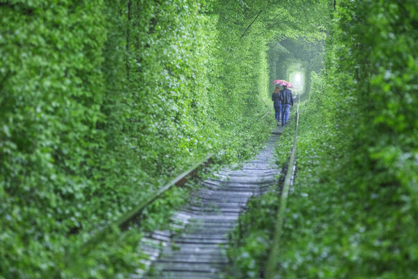 пара под зонтиком, идущая в туннель
