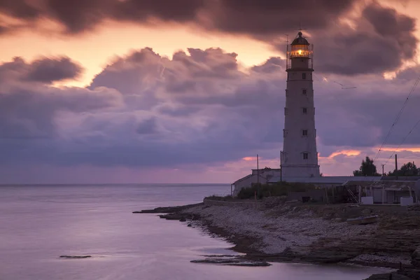 Atardecer de colores y faro de iluminación en la costa del mar Fotos de stock