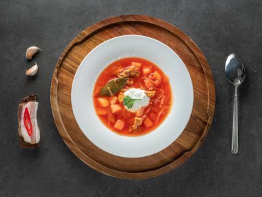 Ekmekte pastırmalı sarımsak ve siyah arka planda siyah ekmek üzerine beyaz tabakta kırmızı Ukrayna borşu.