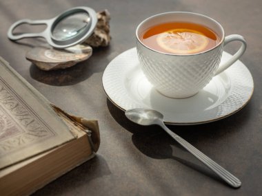 Bir fincan çay, büyüteç ve masanın üzerinde eski bir kitap.