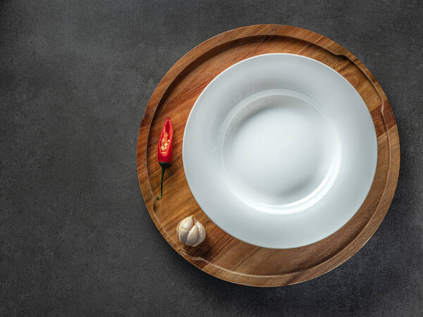 empty white plate on wooden plate and black background with red pepper and garlic