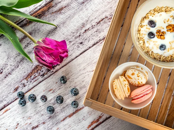 flatlay of breakfest with cereals and colored cakes in wooden box and violet tulip with berries
