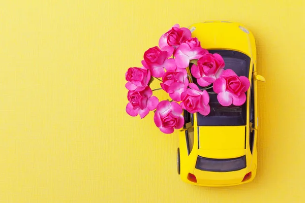 toy car delivering  a bouquet of flowers. Gifts with home delivery concept. Yellow background