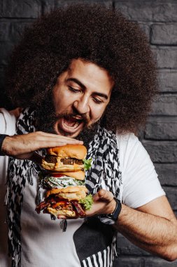 Kıvırcık adam 3 hamburgeri birlikte yemek için ağzını açar. Sağlıklı falafel burger, tuzlu ızgara tavuk ve etli angus burger. Terfi için duygusal fotoğraf