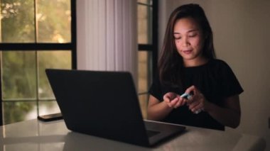 Sosyal mesafeli Asyalı kadın el jeli dezenfektanını eline aldı. Coronavirüsü önlemek için evden çalışacağım. En iyi pencere görünümlü çalışma alanı.