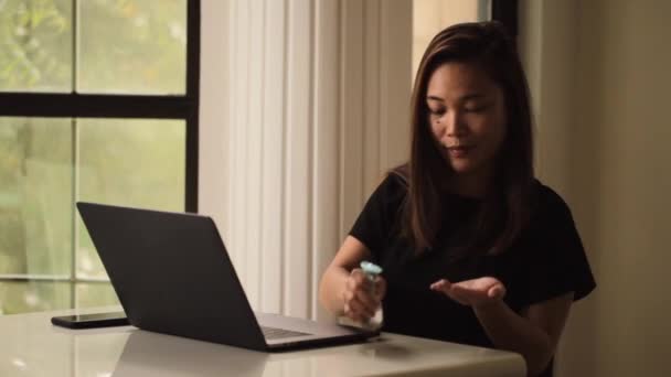 Азиатка, работающая из дома, избегает социального дистанцирования, чтобы бороться с коронавирусом. Фокус работы на ноутбуке с интернетом. Средство для дезинфекции рук на столе . — стоковое видео