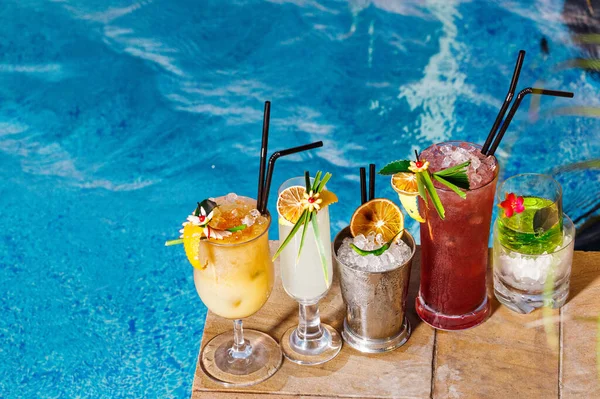 Hotel cocktails and mocktails refreshments  perfect for summer. Beverage photography in pool side of luxury hotel. Fancy drinks decoration with crafted leaf and fruits. Blue clear water.