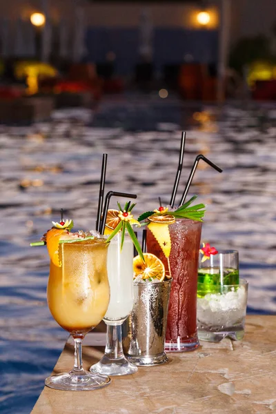 ホテルのカクテルとモッカーは夏に最適です 豪華なホテルのプールサイドでの飲料夜の写真 手作りの葉 オレンジの皮 スライスされた新鮮な果物とファンシードリンクの装飾 — ストック写真