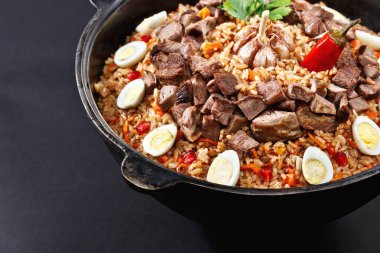 Dilimlenmiş etle yakın plan pilav, bıldırcın yumurtasıyla süslenmiş sarımsak. Aile porsiyonu. Özbek geleneksel tabak manevrası. Koyu arkaplan.
