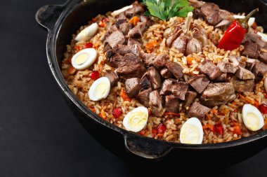 Dilimlenmiş etle yakın plan pilav, bıldırcın yumurtasıyla süslenmiş sarımsak. Aile porsiyonu. Özbek geleneksel tabak manevrası. Koyu arkaplan.
