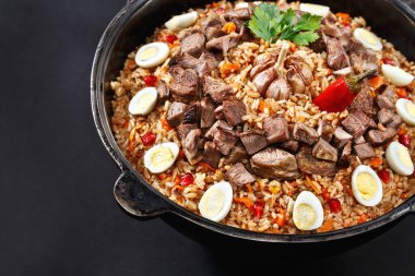Dilimlenmiş etle yakın plan pilav, bıldırcın yumurtasıyla süslenmiş sarımsak. Aile porsiyonu. Özbek geleneksel tabak manevrası. Koyu arkaplan.