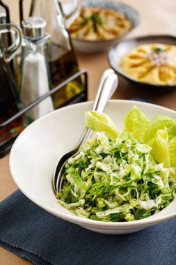 Otantik Yunan mutfağından taze yeşil salata. Arka planda güzel yemek tabağıyla sunulan salata fotoğrafçılığı, Yunan restoran menüsü konsepti için en iyi kavram.