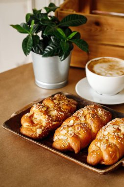 Ahşap bir tepside çeşitli malzemelerle taze pişmiş ekmek. Masa arkasında sıradan bir yemek ve kahve. Otantik Akdeniz mutfağı fotoğrafçılık konsepti.