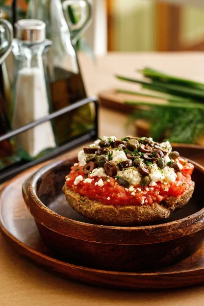 Authehntic greek cuisine fried tomato fritters with greek feta cheese, fresh herbs, oregano, and olives. Presentable appetizer plating on wooden bowl in casual dine in table background.