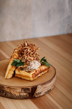 Tahta bir tahtanın üzerinde ince dilimlenmiş soğan gevreği ve beyaz sosla kaplanmış Belçika waffle tabağı. Dergi veya çevrimiçi dağıtım menüsü için yiyecek fotoğrafçılığı kavramı.