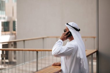Emirati 'nin şehir emirliklerinde geleneksel kandura giyen adamı akıllı telefonla konuşuyor. Arap dergisi için kenar görüş konsepti.
