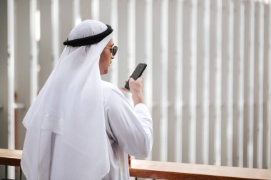 Emirati 'nin şehir emirliklerinde geleneksel kandura giyen adamı akıllı telefonla konuşuyor. Arap dergisi için kenar görüş konsepti.