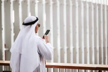Emirati 'nin şehir emirliklerinde geleneksel kandura giyen adamı akıllı telefonla konuşuyor. Arap dergisi için kenar görüş konsepti.