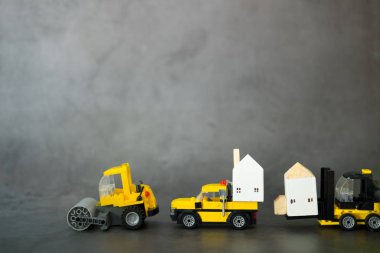 Sarı bir inşaat arabası seti ahşap evler taşıyor.