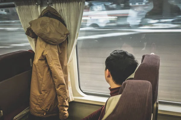 Uomo asiatico che guarda attraverso la finestra con la neve. Viaggia su un treno. — Foto Stock