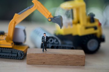 Minyatür insanlar: işadamı sarı oyuncak kazıcısının önünde duruyor. Taşınabilir mülkiyete yatırım analizi.