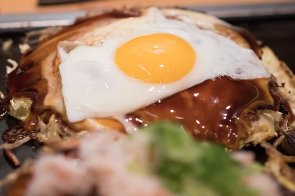 Primer plano de la comida local japonesa llamada okonomiyaki o pizza hiroshima cocinada con huevo y salsa de fideos de cerdo de col mixta — Foto de Stock