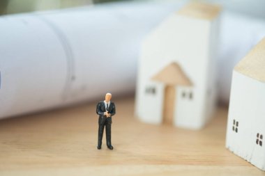 Minyatür ev ve kağıt mimarı planının önünde duran minyatür işadamı. Projeye yapılan ev yatırımlarında liderlik sözleşmesi kavramı