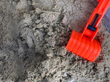 Çocuk kum havuzunda turuncu oyuncak yükleyici oynuyor.