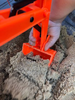 Çocuk kum havuzunda turuncu oyuncak yükleyici oynuyor.