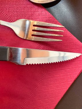 Kırmızı peçetede gümüş bıçak ve çatal.