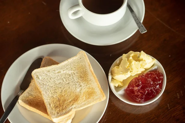 Ontbijt 's morgens sneetjes toast, boter en jam geserveerd met warme koffie op houttafel — Stockfoto