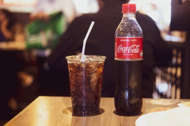 Bangkok, Tayland - 17 Şubat 2020: Yarısı tüketilmiş Coca-Cola şişesi ve bir restoranda buzlu kola