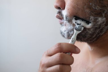 Genç adamın sabahları yüzünü sabun ve krem kullanarak traş edişine yakından bakın.