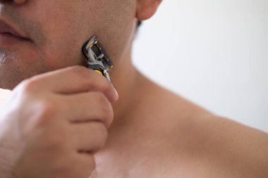 Bir adam tıraş makinesini köpük, sabun ve krem kullanmadan tıraş eder. Kapat.