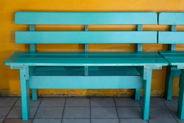 Sarı beton duvarlı yeşil ahşap bank bekliyor.