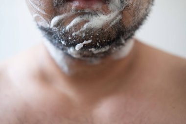 Yüzünde tıraş köpüğü olan, sakallı yakışıklı bir adamın yakın portresi.